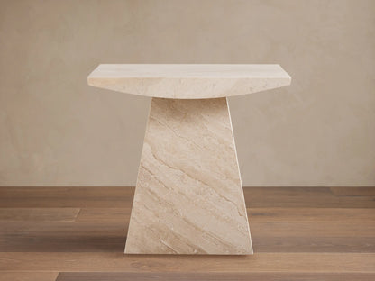 A beige marble side table with a trapezoidal base and a rectangular top, set on a wooden floor against a light wall.