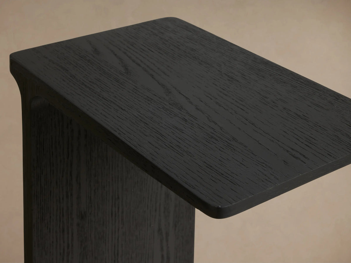 Close-up, angled view of the Ebony Iva C Table, highlighting the red oak veneer's visible wood grain and sculptural frame.