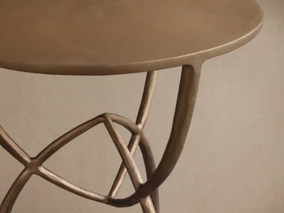 Front view of the gold Jedrek End Table with a round top and curved, intersecting legs with hand-pounded texture.