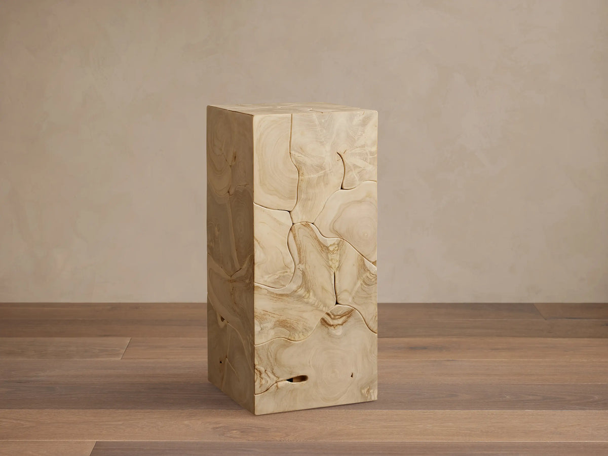 Kalmar Pedestal made of natural teak wood with visible organic shapes, cracks, and patinas, on a wooden floor.
