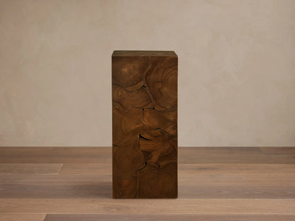 Kalmar Pedestal made of natural teak wood with visible organic shapes, cracks, and patinas. Stands on a wooden floor against a neutral wall.