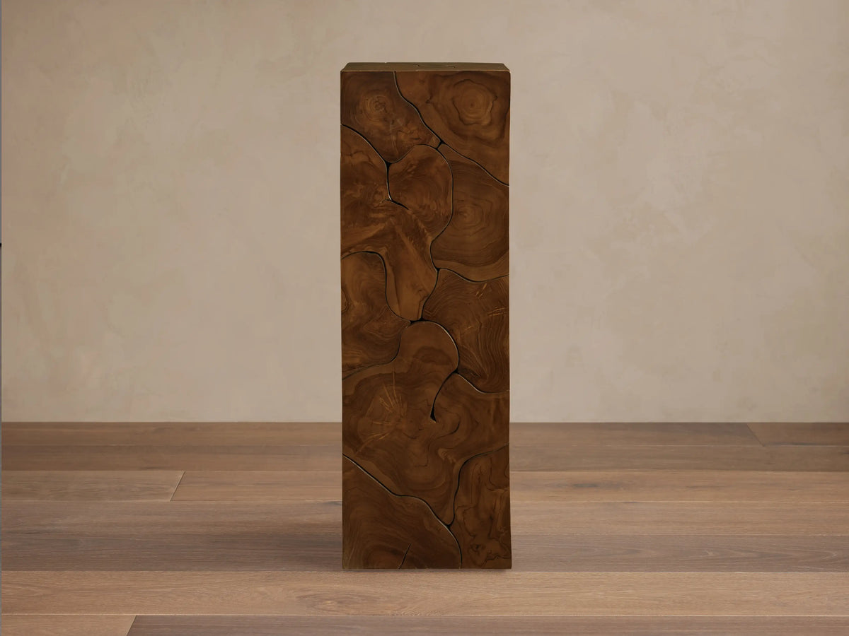 Kalmar Pedestal made from teak wood with visible organic cracks and patterns. It has a tall, rectangular shape with rich wood tones.