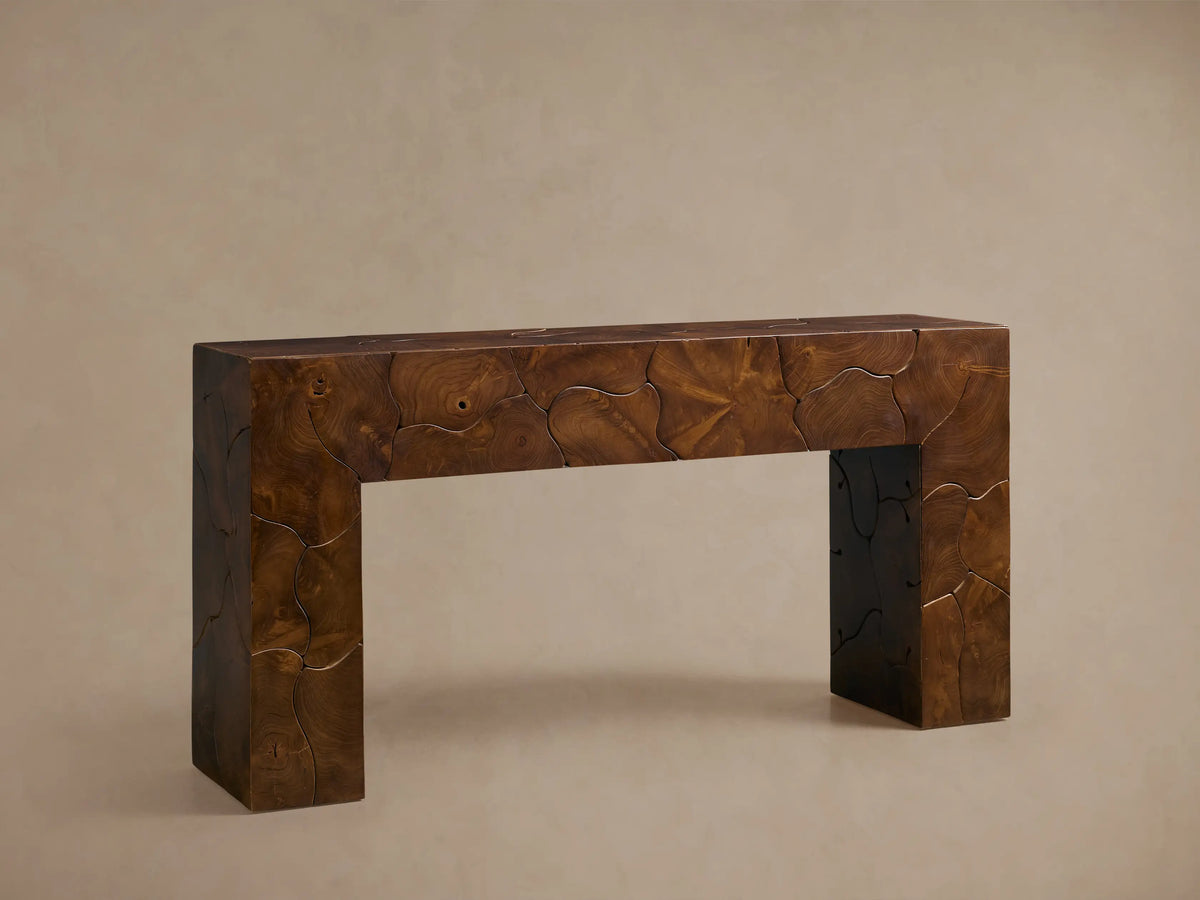 Kalmar Console Table in rich brown wood with organic patterns, decorated with a white vase and books on top, against a beige wall.