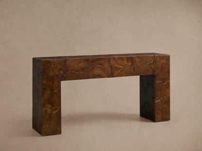Kalmar Console Table in rich brown wood with organic patterns, decorated with a white vase and books on top, against a beige wall.