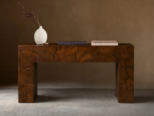 Kalmar Console Table in rich brown wood with organic patterns, decorated with a white vase and books on top, against a beige wall.