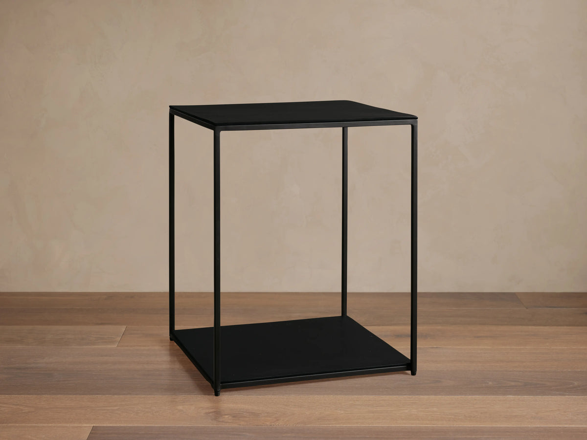 Kavali Square End Table in black, featuring a minimalist design with a solid iron frame and a powder-coated finish, set on wood flooring.