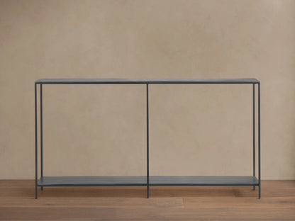 A minimalist Kavali Console Table with a black, powder-coated iron frame, slim design, and two shelves, against a neutral wall.