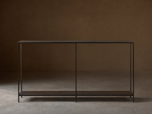 A minimalist Kavali Console Table with a black, powder-coated iron frame, slim design, and two shelves, against a neutral wall.