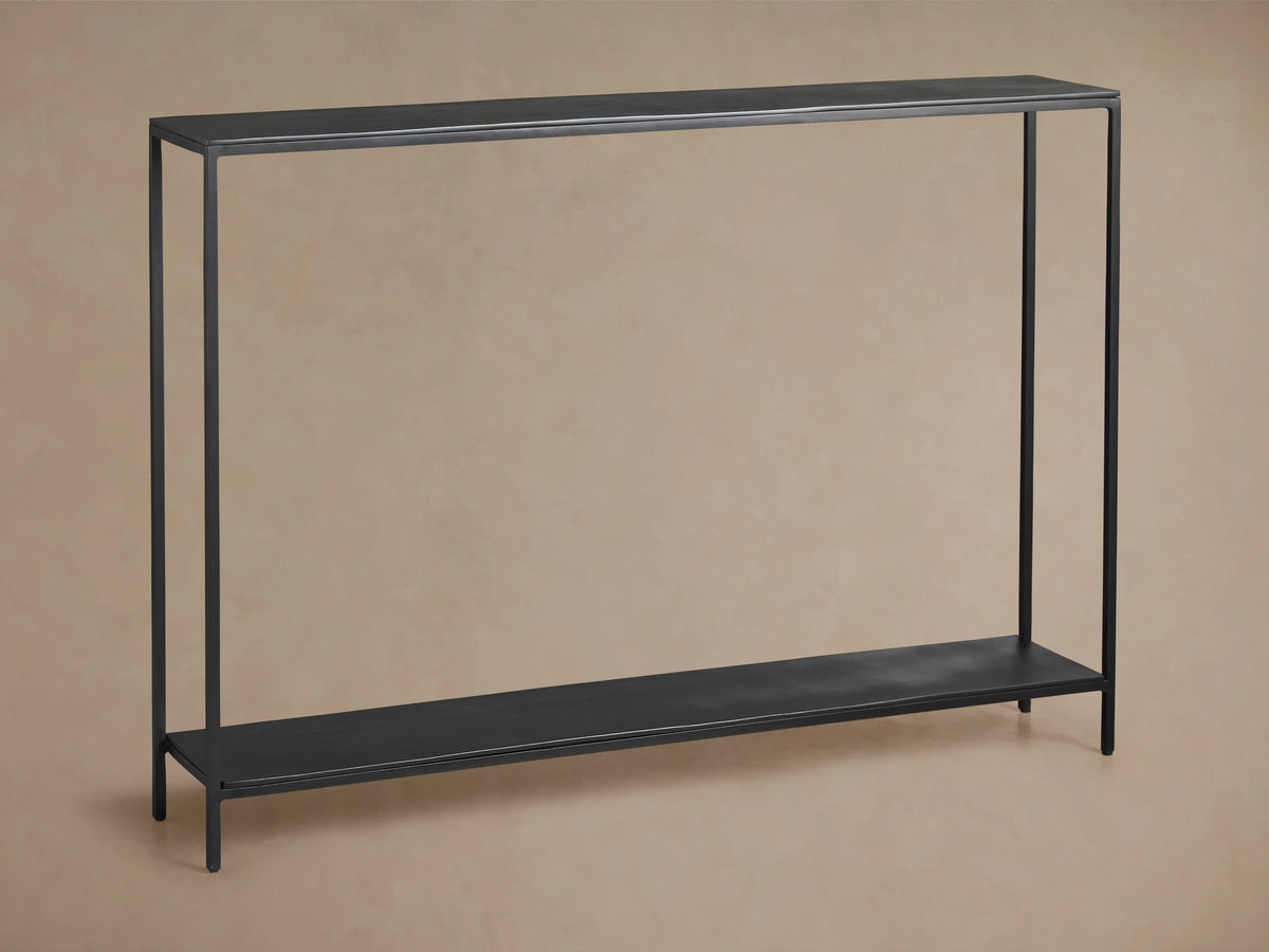 Kavali Slim Console Table, black powder-coated iron frame, rectangular with narrow tabletop and base shelf, on wooden floor.