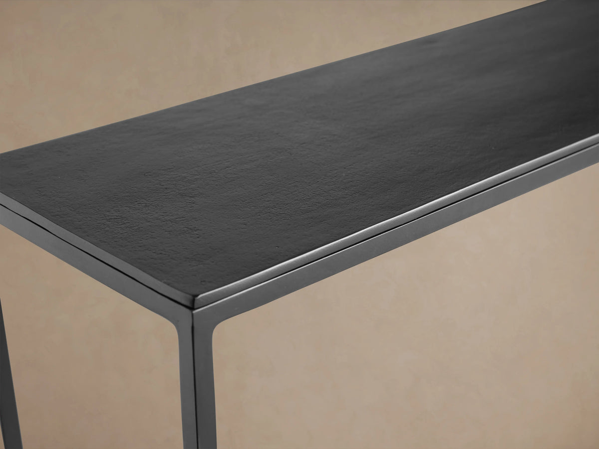 Kavali Slim Console Table in black iron, featuring a minimalist rectangular frame with a lower shelf, against a beige background.