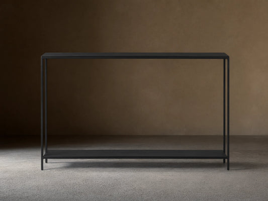 Kavali Slim Console Table, black powder-coated iron frame, rectangular with narrow tabletop and base shelf, on wooden floor.