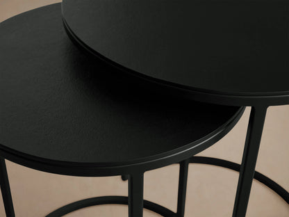 Alt text: Two Kavali Nesting End Tables with round black powder-coated iron frames. The larger table is slightly taller, both set on a wooden floor.
