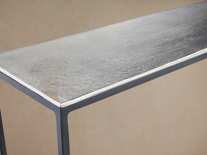 Kavali Slim Console Table with a slim, rectangular aluminum surface featuring a textured, antiqued silver patina on black iron legs.