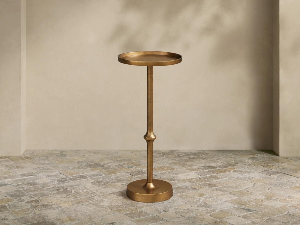 Kenneth Martini Table: Tall, hand-antiqued polished gold cast aluminum with round top, slender stem, and round base. On stone floor.