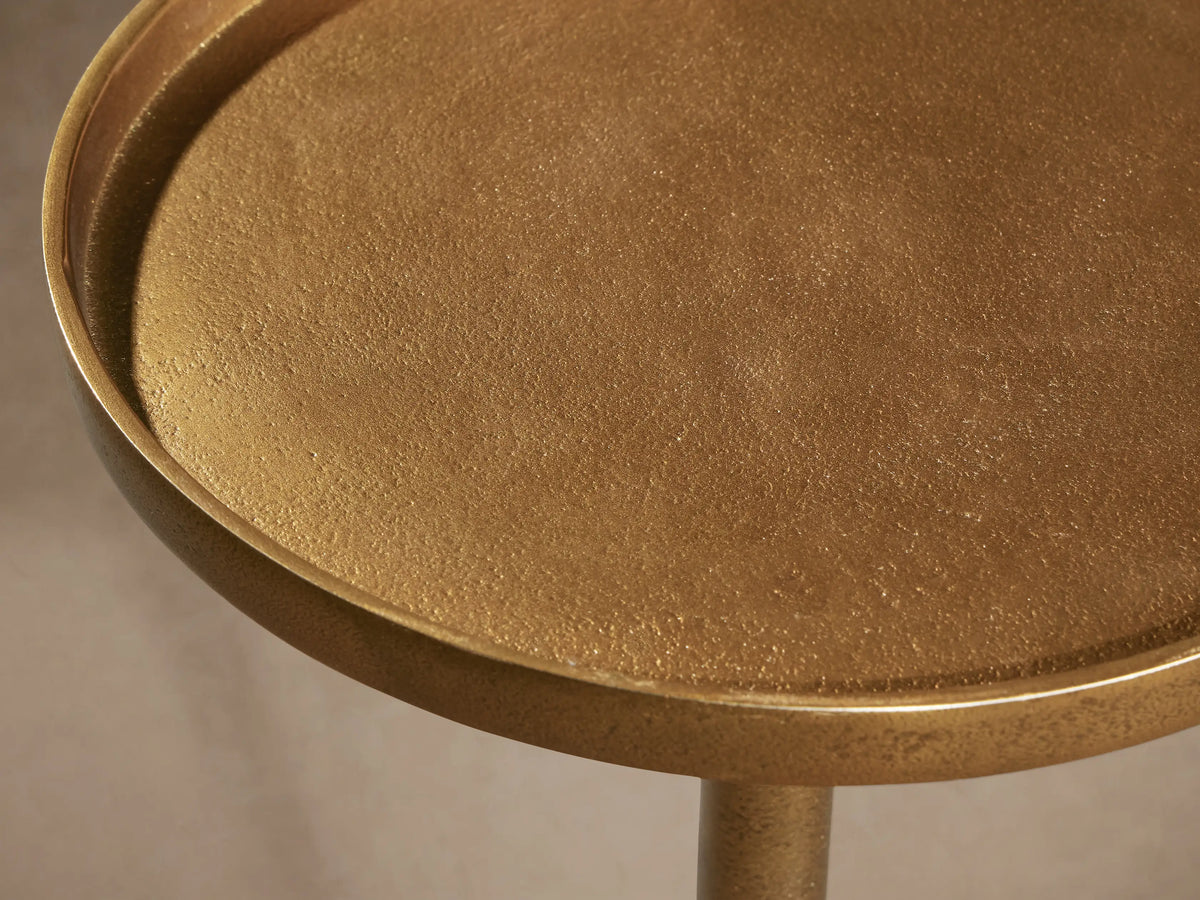 Kenneth Martini Table: a polished, antiqued gold cast aluminum table with round top and base, on a wooden floor.