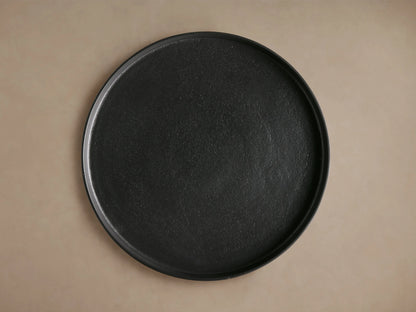 Kenneth Martini Table, top view showing round, dark cast aluminum surface with unique textured finish on a neutral background.