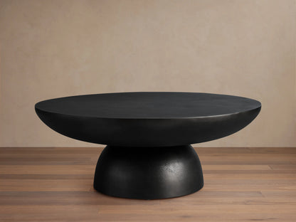 Kyoto Round Coffee Table with smooth black finish, cast from aluminum. Features a wide, rounded top and sturdy base on wooden floor.