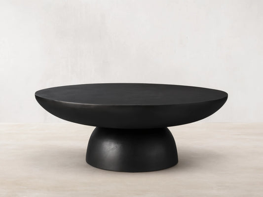 Kyoto Round Coffee Table with smooth black finish, cast from aluminum. Features a wide, rounded top and sturdy base on wooden floor.