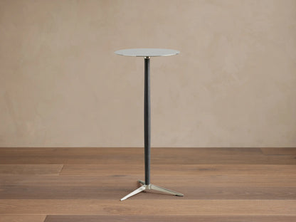 A sleek Lancia Martini Table with a round glass top, slim black leather-wrapped stem, and three-legged stainless steel base.