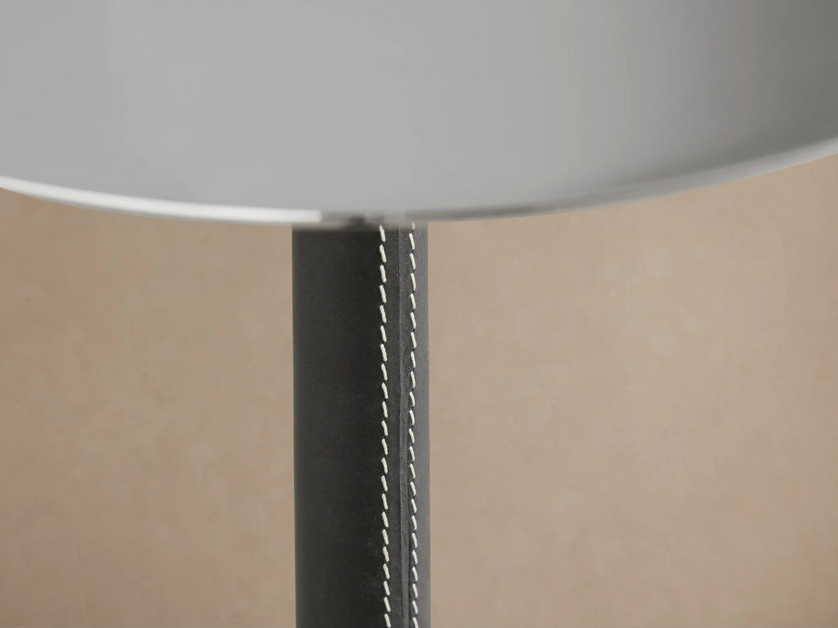 A sleek Lancia Martini Table with a round glass top, slim black leather-wrapped stem, and three-legged stainless steel base.
