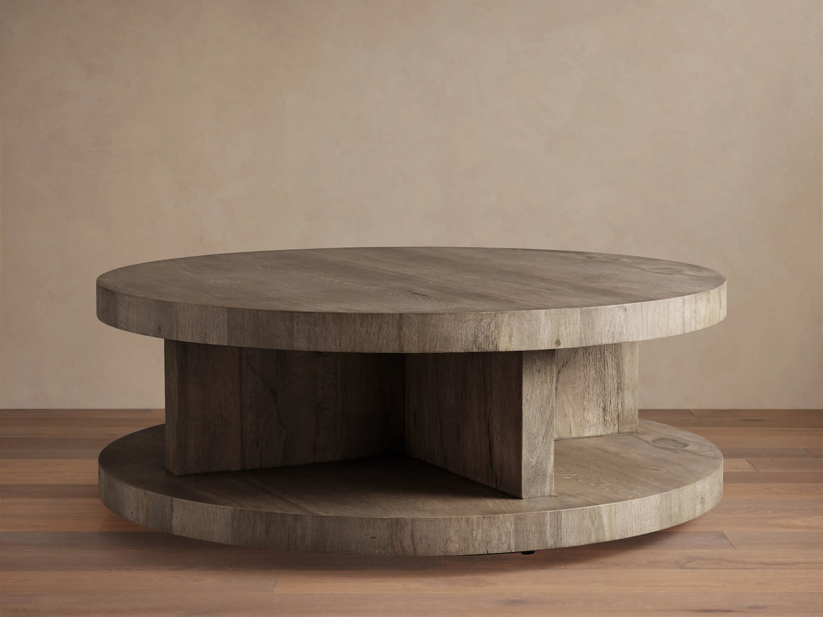 Round coffee table made of reclaimed oak with a natural wood grain texture. Features a flat top and bottom shelf, in a warm, light wood tone.