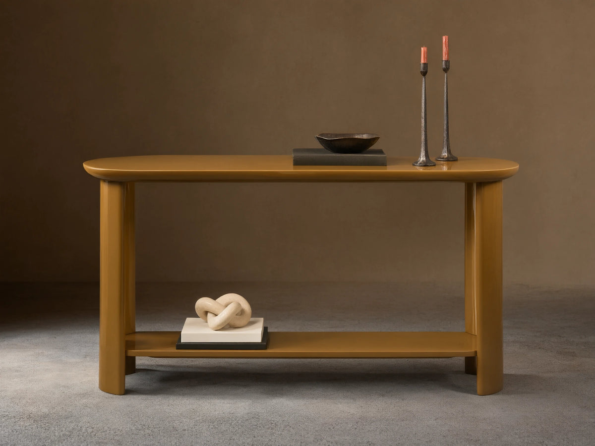High-gloss camel Lonny Console Table with rounded oval top, thick legs, & floating lower shelf. Candles, bowl, books on top & decor on shelf.