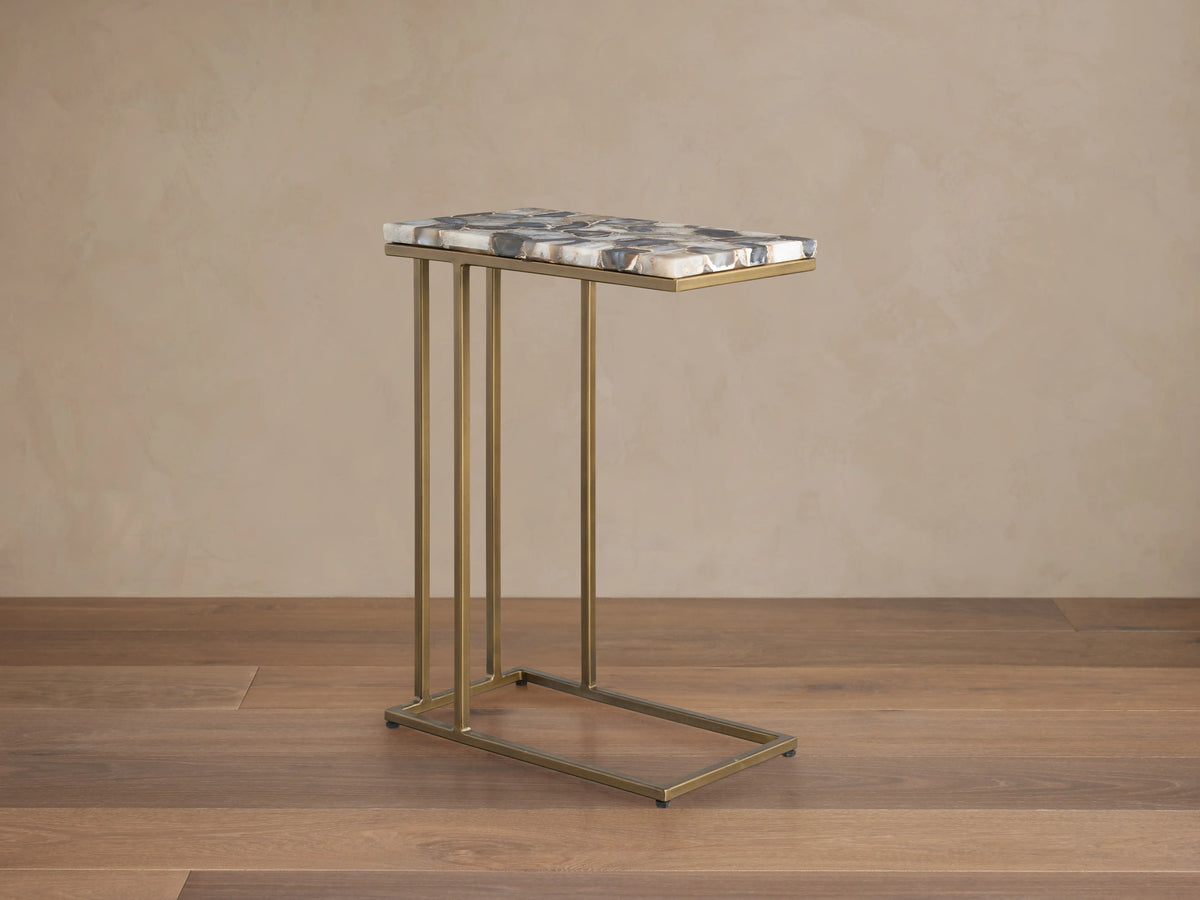 Ludlow C Table with a hand-cut stone top in various shades and a slim, iron base with an antiqued finish, placed on a wooden floor.