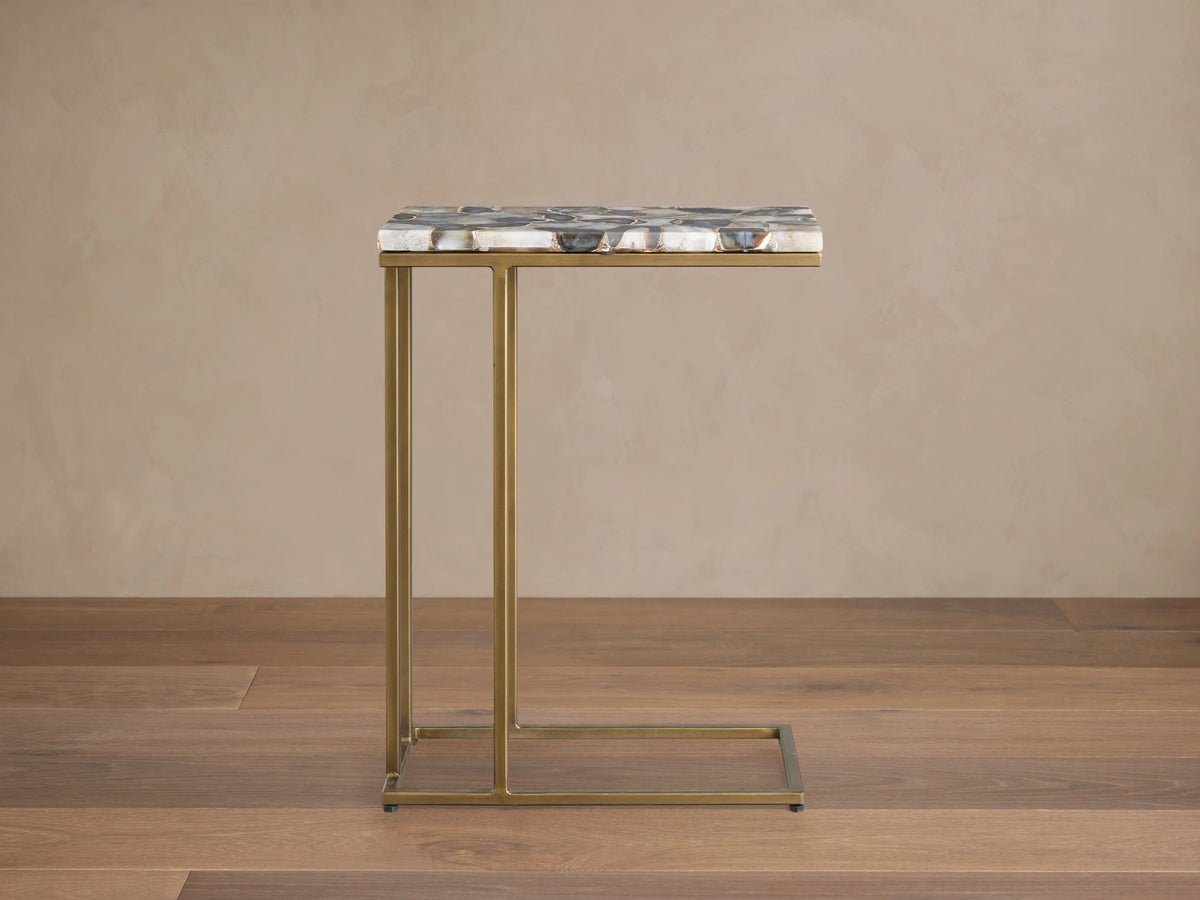 Ludlow C Table with a multicolored stone tabletop and slender, antiqued brass iron base, shown on a wooden floor.