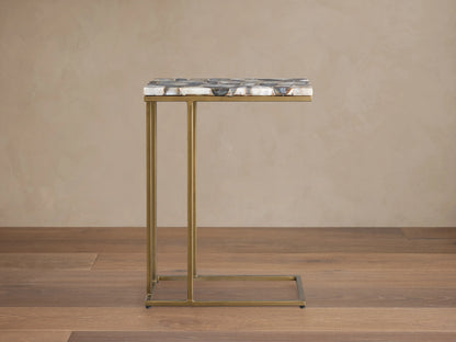 Ludlow C Table with a multicolored stone tabletop and slender, antiqued brass iron base, shown on a wooden floor.