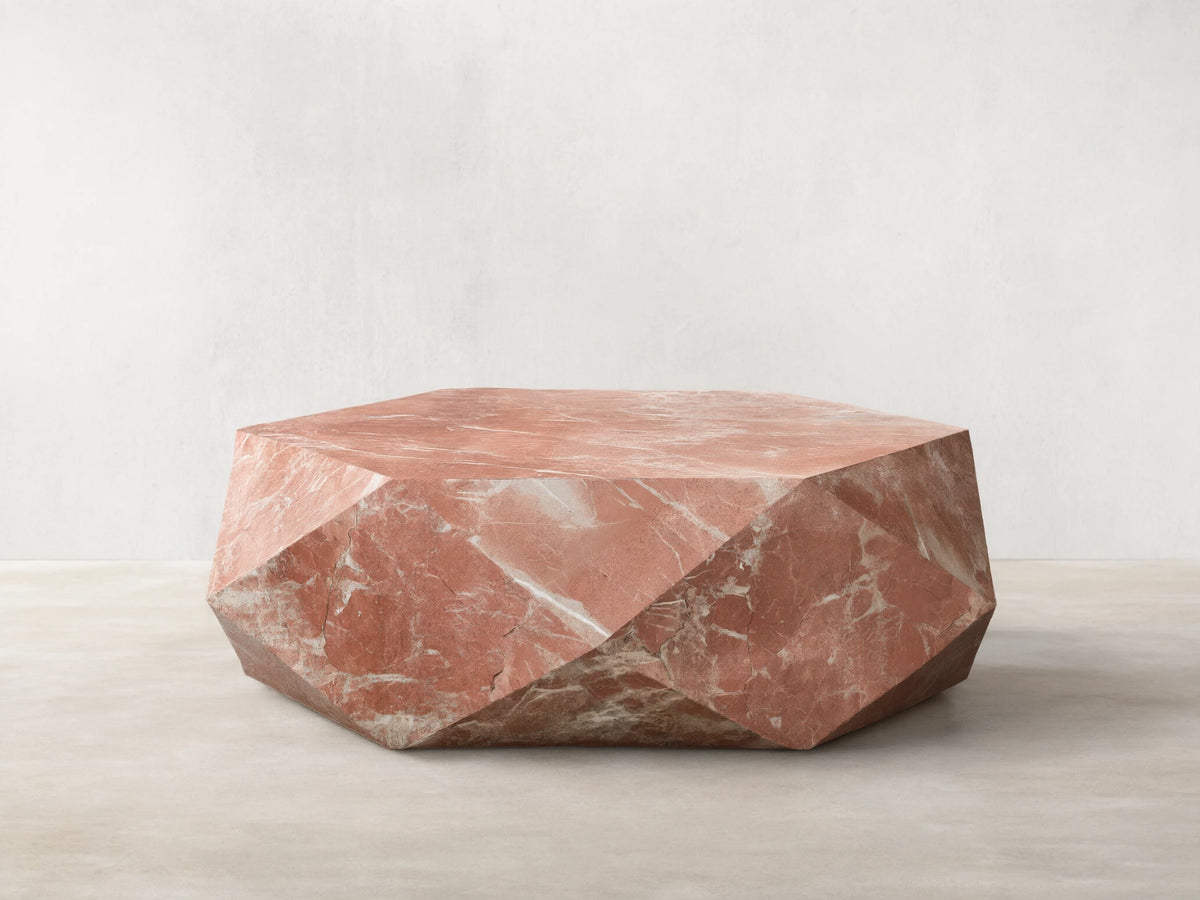 Front view of a faceted, hexagonal coffee table made of pink marble with white veins.