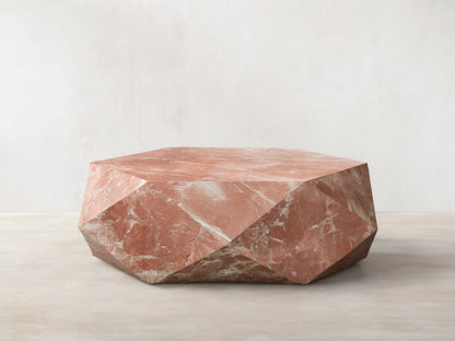 Front view of a faceted, hexagonal coffee table made of pink marble with white veins.