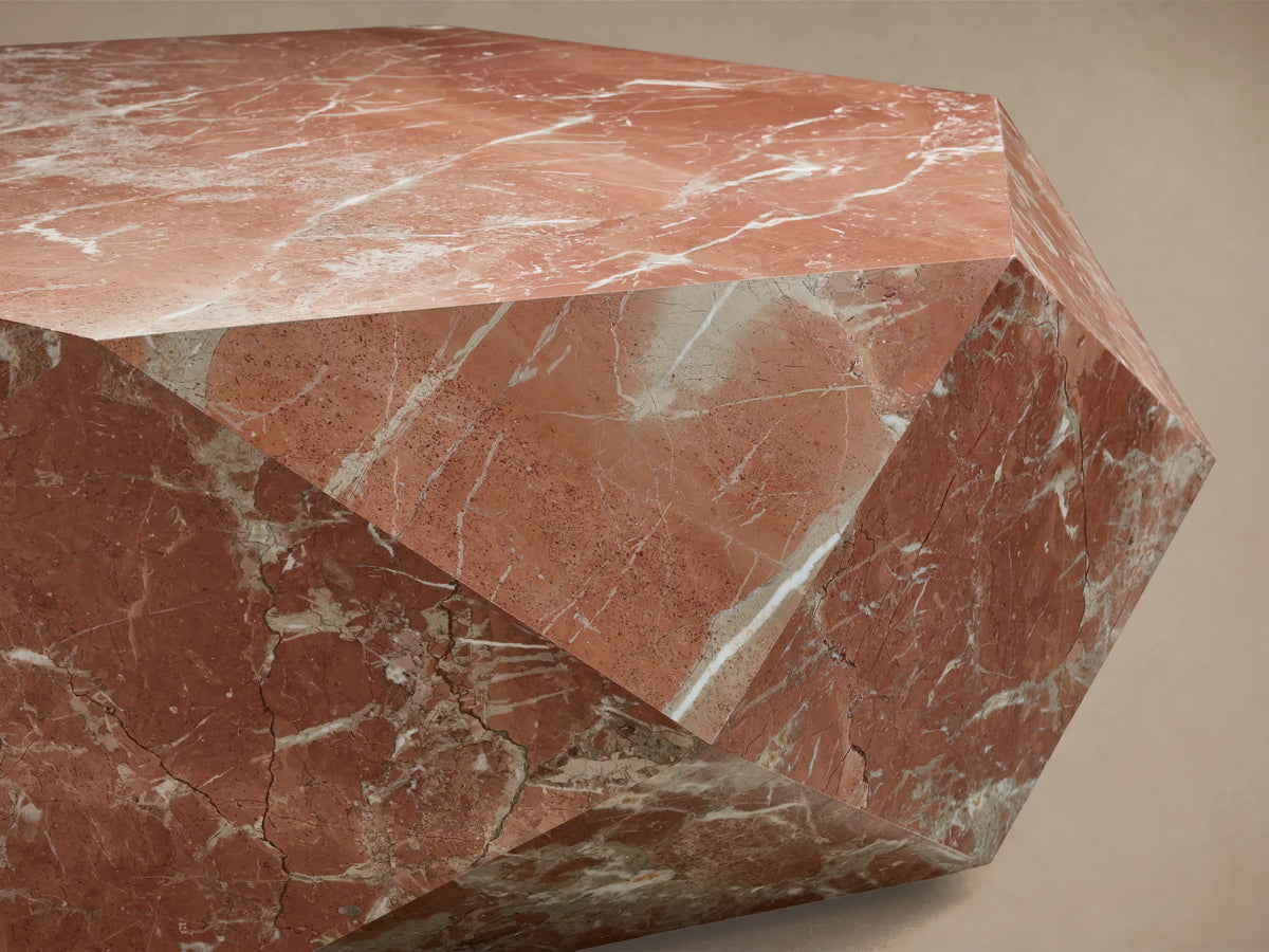 Close-up of a geometric, multifaceted object crafted from reddish-brown marble with white and gray natural veining.