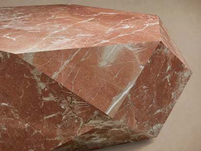 Close-up of a geometric, multifaceted object crafted from reddish-brown marble with white and gray natural veining.