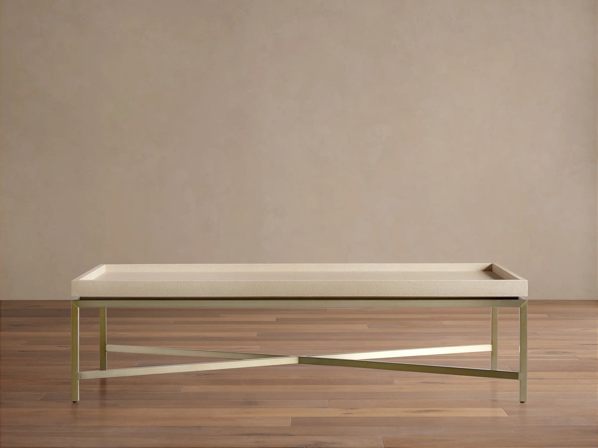 Malone Coffee Table with light beige shagreen leather tabletop and gold metal X-base, centered on a wooden floor.