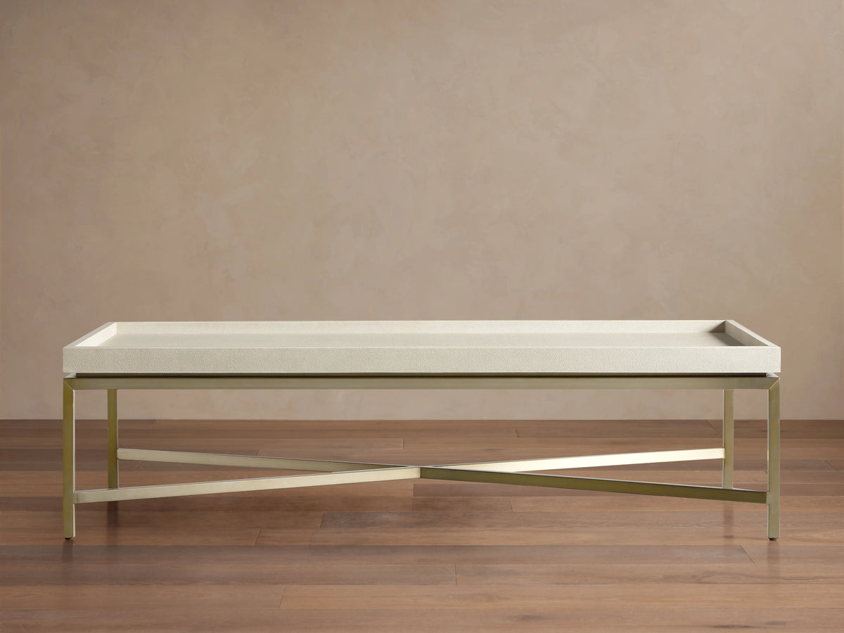 Malone Coffee Table with light beige shagreen leather top, supported by a champagne gold steel base, angled on a beige background.