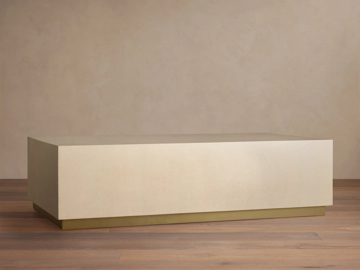 Malone Plinth Coffee Table, rectangular, light beige shagreen top, and slim brass plinth base on a wooden floor.
