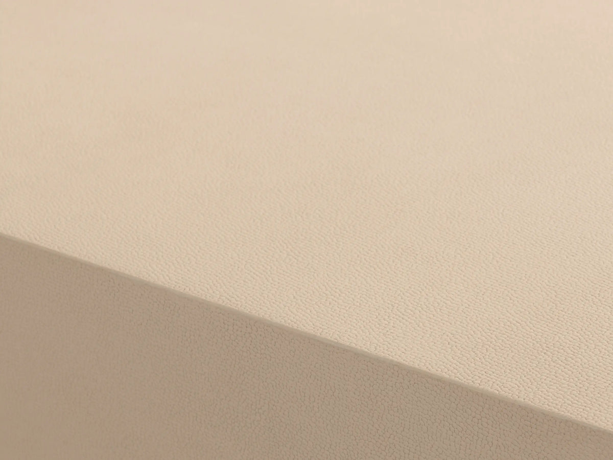 Malone Plinth Coffee Table with a textured light beige top & sides, on a thin brass-finished steel base. On wood floor.