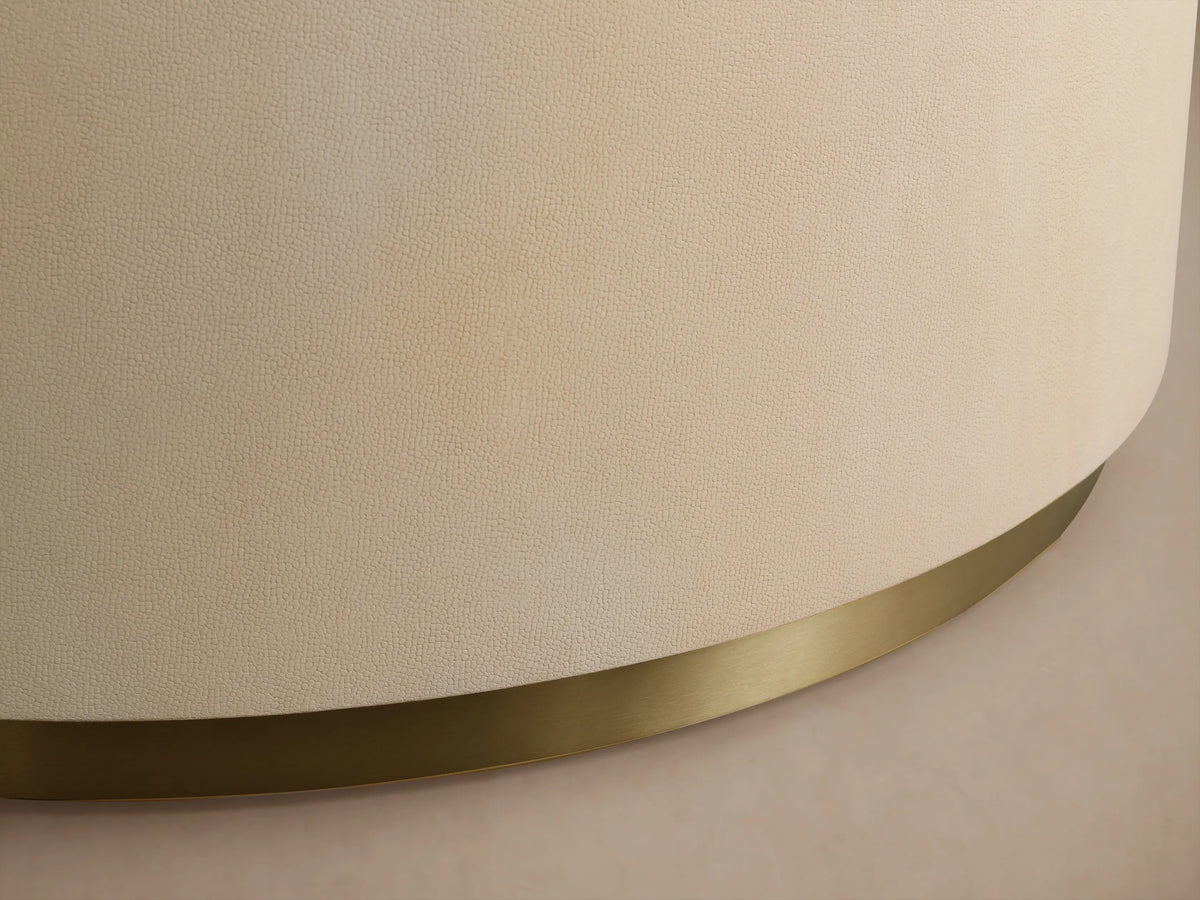 Malone Round Plinth Coffee Table: Cream, round, textured plinth-style coffee table with a golden brass base, on wood floor.