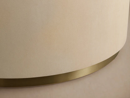 Malone Round Plinth Coffee Table: Cream, round, textured plinth-style coffee table with a golden brass base, on wood floor.