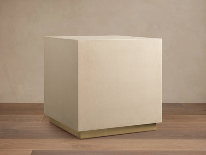 Malone Square Plinth End Table, light beige shagreen textured cube with a thin brass base, against a neutral wall & wood floor.