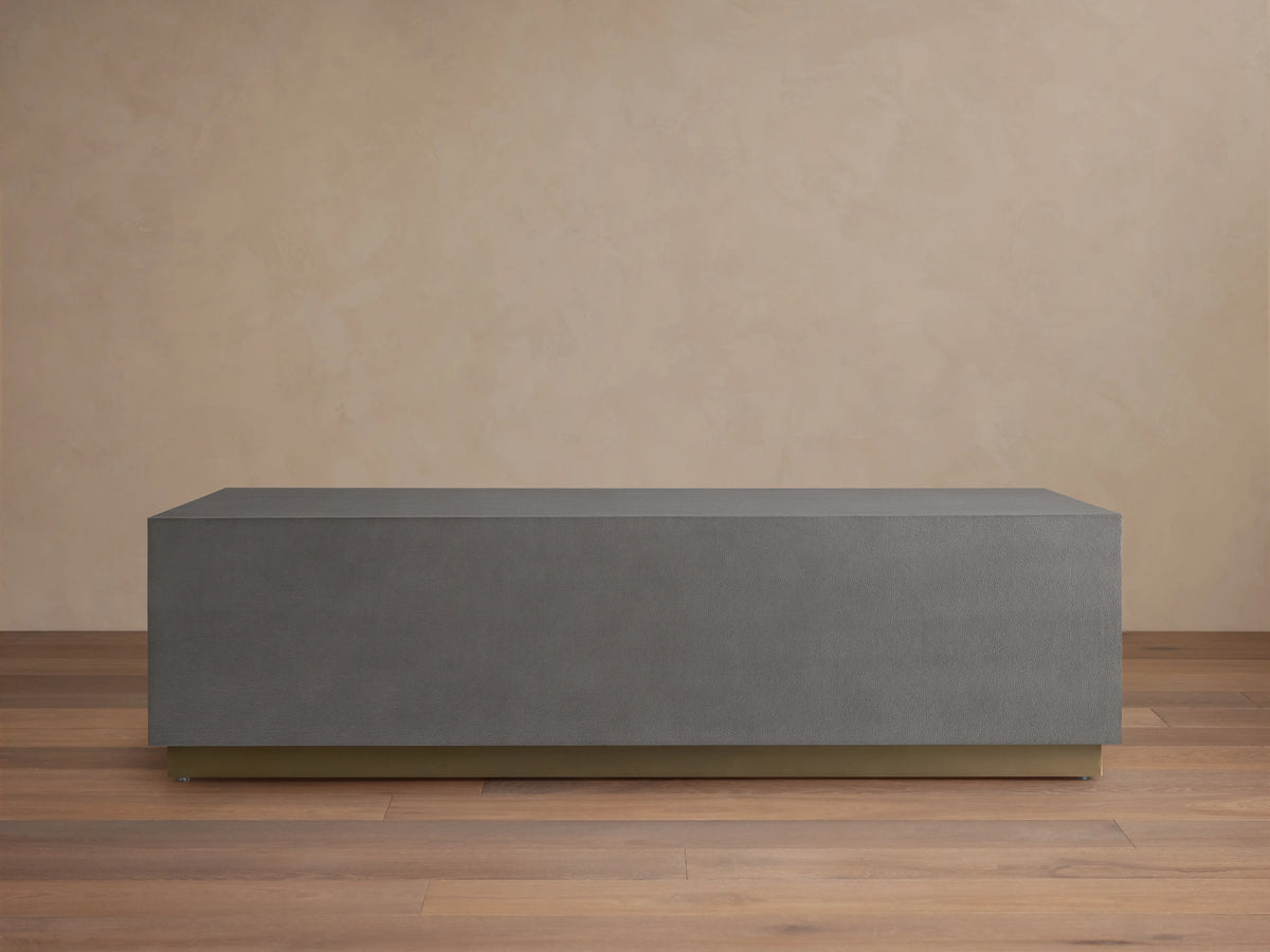 Malone Plinth Coffee Table with a rectangular shape, gray shagreen-patterned surface, and a brass-finished steel base, on wooden flooring.