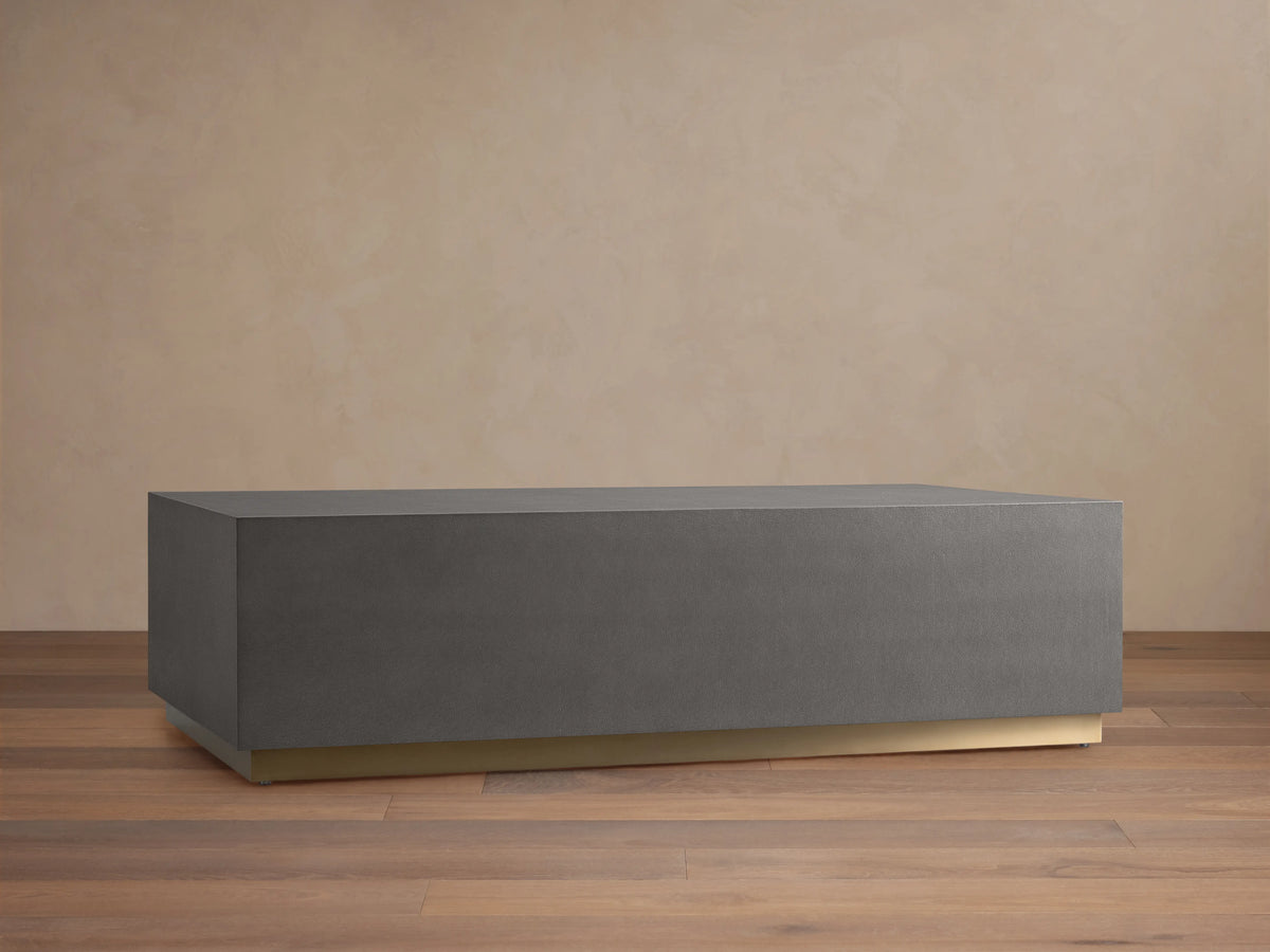 Malone Plinth Coffee Table with a rectangular shape, gray shagreen-patterned top, and a subtle brass-finished base on wooden floor.