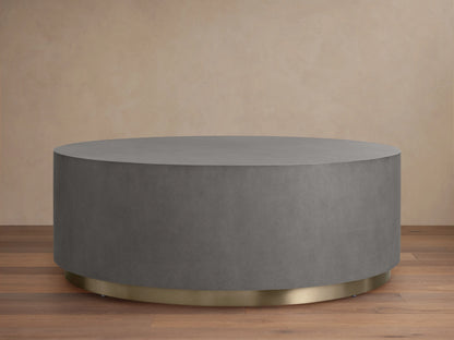 Round plinth coffee table with shagreen-patterned grey top, brass-finished steel base. Placed on wooden floor, beige background.