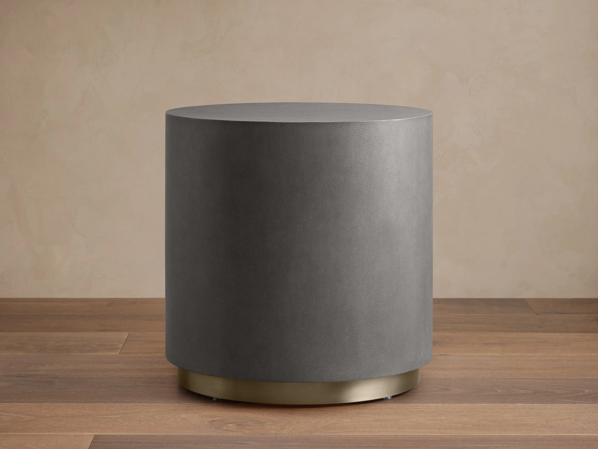 Malone Round Plinth End Table with a dark gray leather-look shagreen cylinder body and a gleaming brass base.
