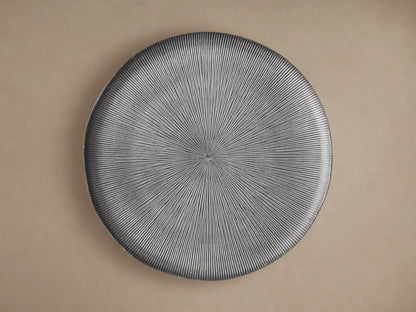 Manhattan Martini Table, close-up of dark grey round top with white-washed radial texture, smooth base, against a beige wall.
