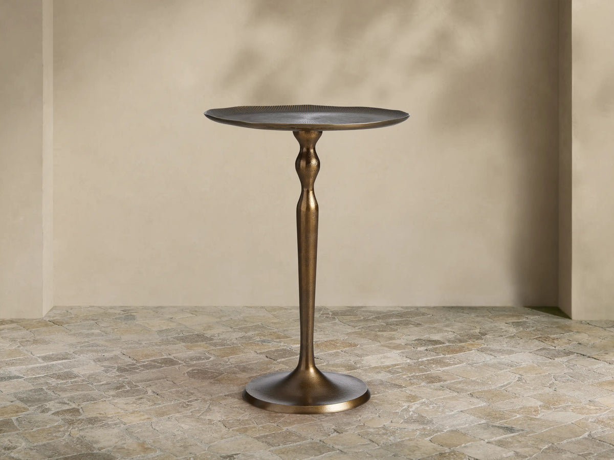 Manhattan Martini Table, dark antique brass finish with a sculpted pedestal base and round textured top, on a tiled floor.