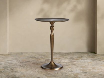 Manhattan Martini Table, dark antique brass finish with a sculpted pedestal base and round textured top, on a tiled floor.