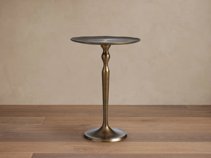 Manhattan Martini Table, dark antique brass finish with a sculpted pedestal base and round textured top, on a tiled floor.