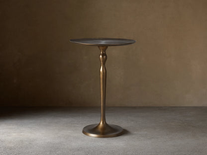 Manhattan Martini Table, dark antique brass finish with a sculpted pedestal base and round textured top, on a tiled floor.