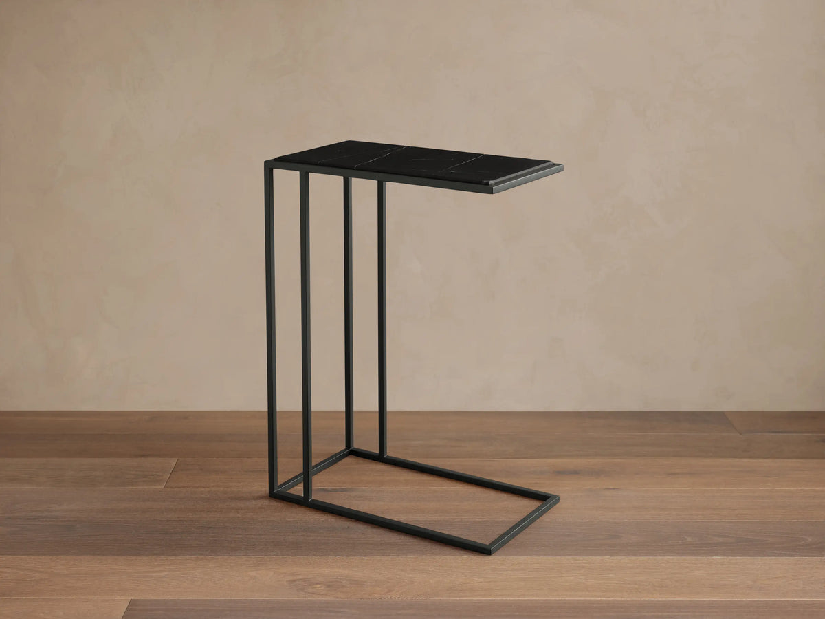 Mills Stone C Table: Matte black C-style steel frame supports a rectangular dark stone top with subtle natural veining on a wood floor.